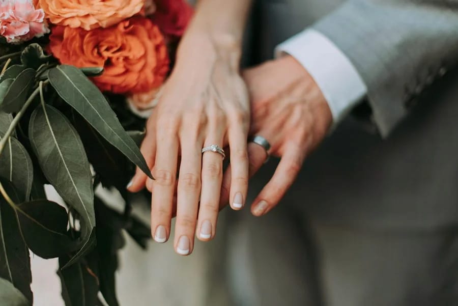 Dua tangan berhias cincin bersenggolan di atas buket bunga oranye